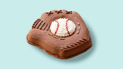 Baseball-shaped cake with baseball on top, placed on a blue surface.