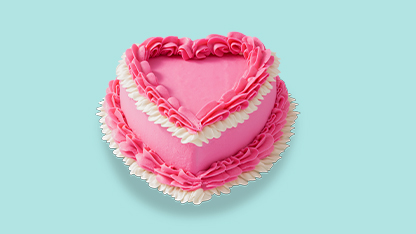A pink heart-shaped cake with white frosting and sprinkles, set on a table.
